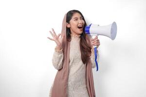 atractivo joven asiático musulmán mujer en velo hijab gesticulando Okay bueno, bueno firmar con su dedos mientras gritos a megáfono. Ramadán y eid Mubarak concepto foto