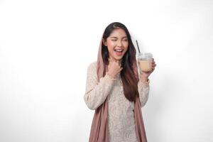 retrato de un emocionado joven asiático mujer levantamiento puño arriba gesto, victorioso y celebrando victoria actitud mientras participación café en un el plastico taza. Ramadán y eid Mubarak concepto foto