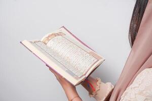 Close up portrait of Asian Muslim woman in headscarf veil hijab holding and reading Al Quran over isolated white background. Ramadan and Eid Mubarak concept. photo