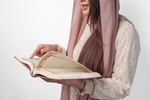 Close up portrait of Asian Muslim woman in headscarf veil hijab holding and reading Al Quran over isolated white background. Ramadan and Eid Mubarak concept. photo