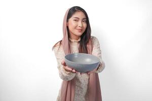 contento asiático musulmán mujer participación cuenco y cuchillería a comer después rápido mientras sonriente alegremente en aislado blanco antecedentes. Ramadán concepto foto