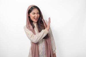 Young Asian Muslim woman wearing veil hijab gesturing a no rejection, refuse using hands and fingers, isolated by white background. Ramadan and Eid Mubarak concept photo