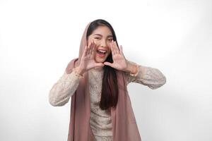 Young Asian Woman wearing headscarf veil hijab is raising hands and shouting with mouth wide open, isolated white background photo