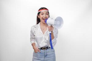 Energetic Asian woman in casual formal outfit wearing country flag headband while holding and shouting at megaphone, standing on isolated white background photo