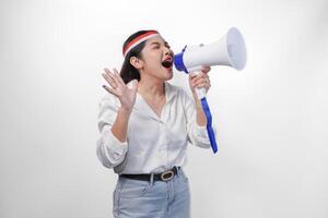 Energetic Asian woman in casual formal outfit wearing country flag headband while holding and shouting at megaphone, standing on isolated white background photo