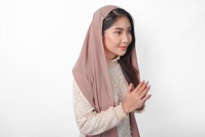 Smiling young Asian Muslim woman gesturing Eid Mubarak greeting from side view isolated over white background photo