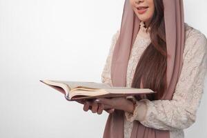 Close up portrait of Asian Muslim woman in headscarf veil hijab holding and reading Al Quran over isolated white background. Ramadan and Eid Mubarak concept. photo