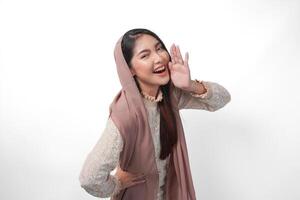 joven asiático mujer vistiendo Pañuelo velo hijab es levantamiento manos y gritos con boca amplio abierto, aislado blanco antecedentes foto
