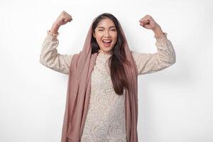 Young Asian woman in headscarf veil hijab full of confidence raising a fist up hand sign gesture, displaying a strong girl pose. Ramadan concept photo