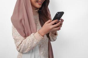 Close up portrait of Asian Muslim woman in headscarf veil hijab holding and using smartphone over isolated white background. Ramadan and Eid Mubarak concept. photo