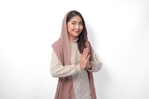 Beautiful Asian Muslim woman wearing headscarf veil hijab smiling to the camera and gesturing traditional greeting isolated over white background photo