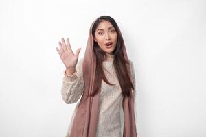 Portrait of attractive Asian Muslim woman wearing veil hijab giving number one to ten by hand gesture, standing over isolated white background photo