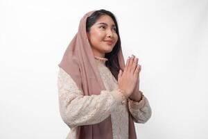 Smiling young Asian Muslim woman gesturing Eid Mubarak greeting from side view isolated over white background photo