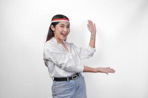 Excited Asian woman wearing flag headband presenting and pointing at the copy space on the side, smiling wide and standing on isolated white background. Independence day advertisement concept photo