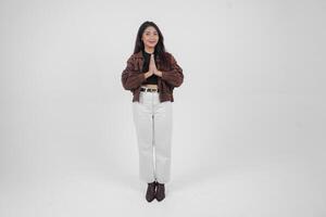 un lleno cuerpo retrato de asiático joven mujer con casual atuendo haciendo saludo gesto con dos manos mientras sonriente, en pie en aislado blanco antecedentes foto