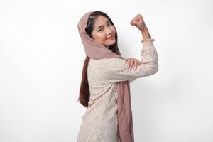 Young Asian woman in headscarf veil hijab full of confidence raising a fist up hand sign gesture, displaying a strong girl pose. Ramadan concept photo