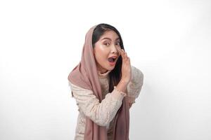 Young Asian Woman wearing headscarf veil hijab is raising hands and shouting with mouth wide open, isolated white background photo