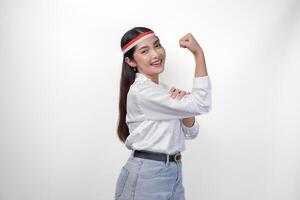 Young Asian woman full of confidence raising a fist up hand sign gesture, wearing flag headband and white shirt, displaying a strong girl pose. Independence day concept photo