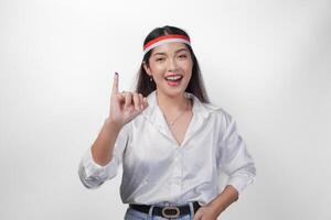 joven asiático mujer con orgullo demostración pequeño dedo sumergido en púrpura tinta después votación para presidente y parlamento elección, expresando emoción y felicidad, vistiendo bandera venda y blanco camisa foto