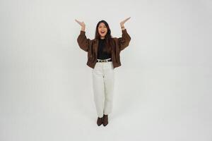 Happy Asian woman wearing casual clothes smiling while pointing up at a copy space, standing at isolated white background photo