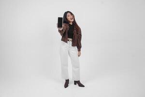 Young Asian woman smiling wide looking happy and holding smartphone while wearing casual outfit standing on isolated white background photo