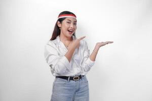 Excited Asian woman wearing flag headband presenting and pointing at the copy space on the side, smiling wide and standing on isolated white background. Independence day advertisement concept photo