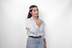 Beautiful Asian woman wearing flag headband with fist on chest celebrating Indonesia Independence Day, standing over isolated white background. Independence day advertisement concept photo