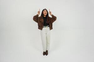 Happy Asian woman wearing casual clothes smiling while pointing up at a copy space, standing at isolated white background photo