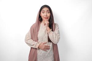 Portrait of Asian Muslim woman wearing headscarf veil placing hands on the stomach feeling hungry and want to eat while fasting, isolated over white background. Ramadan and Eid Mubarak concept photo