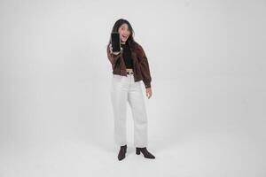 Young Asian woman smiling wide looking happy and holding smartphone while wearing casual outfit standing on isolated white background photo