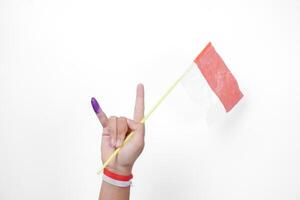 Group of hand wearing flag ribbon on wrist showing little finger dipped in purple ink after voting for Indonesia Election or Pemilu while holding mini flag, isolated over white background photo