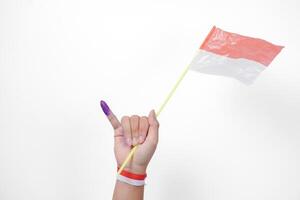 Group of hand wearing flag ribbon on wrist showing little finger dipped in purple ink after voting for Indonesia Election or Pemilu while holding mini flag, isolated over white background photo