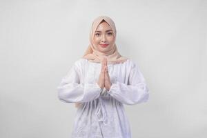 Beautiful Asian Muslim woman wearing white dress and hijab smiling while doing formal welcome or greeting gesture, standing over isolated white background photo