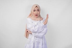 Young Asian Muslim woman wearing hijab and white dress gesturing a no rejection, refuse using hands to the copy space on left side, isolated by white background. Ramadan and Eid Mubarak concept photo