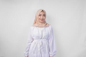atractivo asiático musulmán mujer en blanco vestir y hijab sonriente a el cámara mientras en pie formalmente terminado aislado blanco antecedentes foto