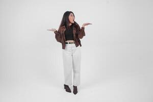 Shocked young Asian girl wearing brown jacket is standing and pointing to a copy space beside her. photo
