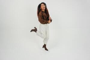 Active Asian girl is jumping and raising hands up wear brown jacket, isolated white color background photo