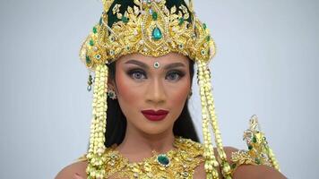 Porträt von ein Frau im traditionell Süd-Ost asiatisch Kostüm mit kompliziert Gold Kopfbedeckung und Schmuck, posieren gegen ein Weiß Hintergrund. video