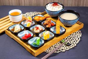 Assorted japanese food Mentaiko Chicken Wings, noodles soup, fried shrimp, sauce, ladyfinger vegetable and pork slice with chopsticks served on wooden board isolated on napkin side view on table photo