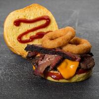 Special burger include beef patty, brisket and onion rings with with melted cheese and mayonnaise isolated on dark grey background side view of fast food sandwich photo