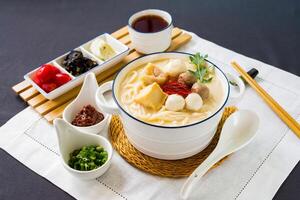 pescado udon en grueso pescado sopa con adolorido cebolla, chile salsa y palillos servido en cuenco aislado en servilleta lado ver de japonés comida en mesa foto