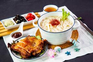 Crispy Grilled Chicken Steak, Fish Udon in Rich Fish Soup noodles served in bowl with chili sauce and chopsticks isolated on napkin side view of japanese foo on table photo