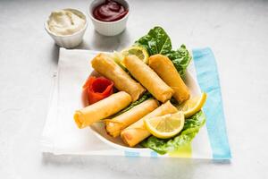 Deep fried Spring Roll with lemon slice and dip sauce served in dish isolated on table top view of arabic food photo