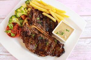 T BONE STEAK with french fries, mayo dip, tomato, broccoli and cucumber salad served in dish isolated on table closeup top view of fastfood spices food photo