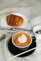 Hot Macchiato Coffee Latte Art served in cup with croissant, puff pastry, bread and knife isolated on napkin side view cafe breakfast photo