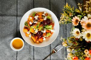 Roasted Vegetables, Feta Crumble and Citrus Salad served in bowl with flowers and fork isolated on napkin top view of healthy green food on table photo