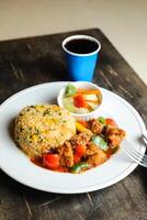 Chili Chicken Rice Meal served in plate with sauce, cold drink, spoon and fork isolated on wooden board side view of thai food photo