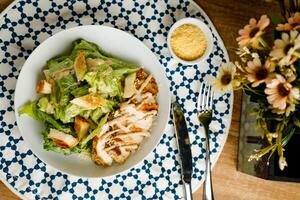 Caesar Salad or ceaser include chicken and spinach served in plate with flowers, knife and fork isolated on napkin top view of healthy green food on table photo