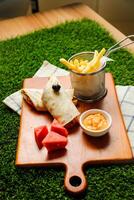 Chipotle Chicken Egg wrap roll filled with tomato, onion, cucumber, cheese with french fries, mayo dip and watermelon slice served on wooden board top view of fastfood appetizer photo