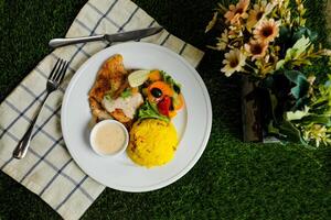 Grilled Jerk Spiced Fillet Fish with rice, dip and salad served in plate with knife and fork isolated on napkin top view of korean style meat food on gassy background photo